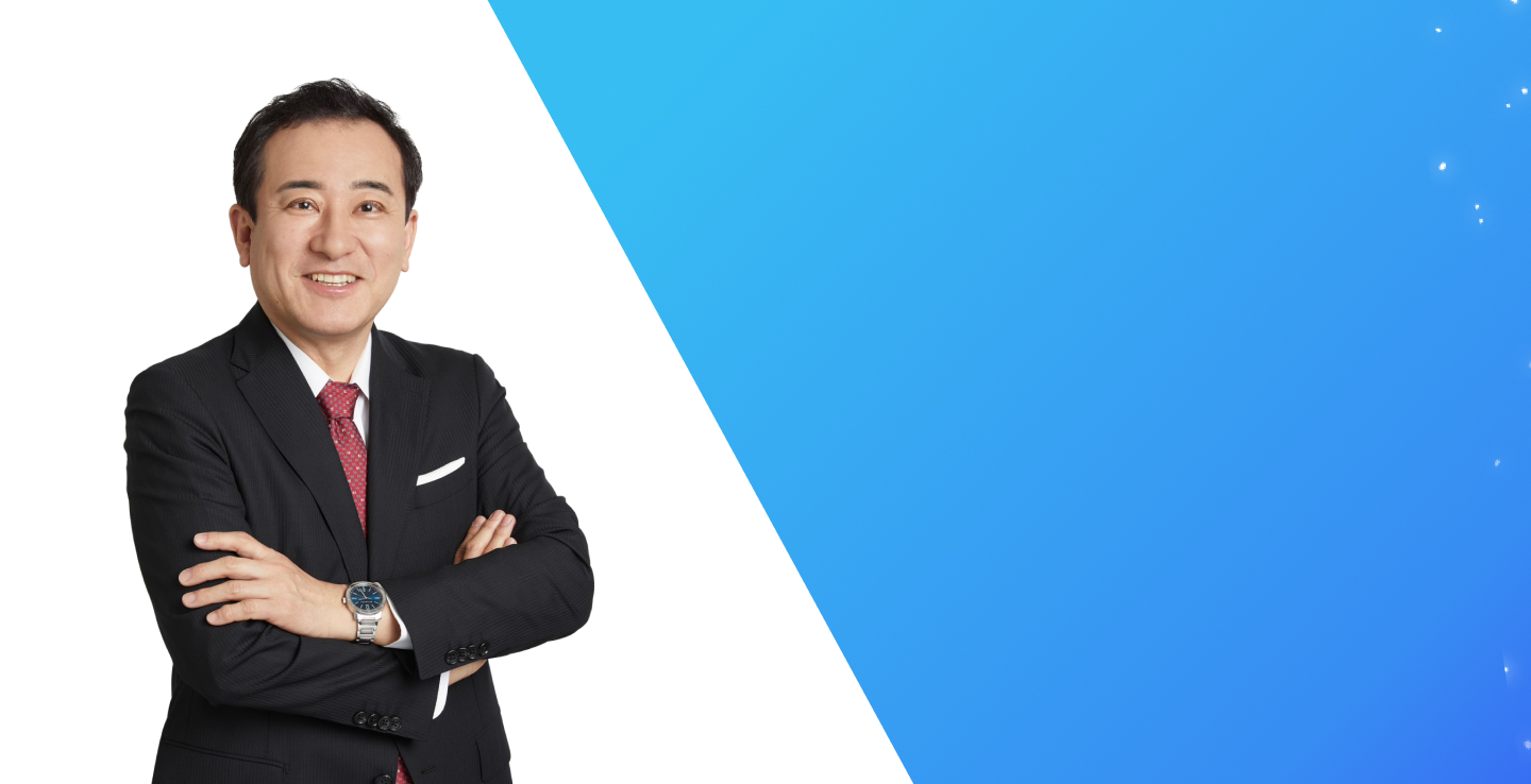 ジャーナリストで大学教授のこにしかずよしさんのプロフィール写真。青いグラデーション背景に笑顔で腕を組んで立っている。