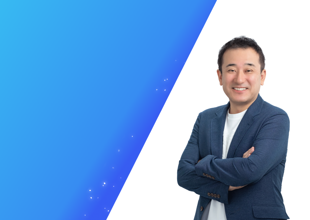 ジャーナリストで大学教授のこにしかずよしさんのプロフィール写真。青いグラデーション背景に笑顔で腕を組んで立っている。